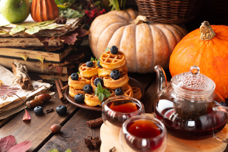 many waffles are stacked on a plate, decorated with mint leaves and blueberries. Tea in a glass teapot and two small bowls.の写真素材