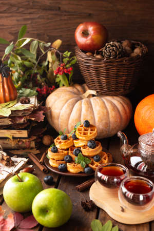 many waffles are stacked on a plate, decorated with mint leaves and blueberries. Tea in a glass teapot and two small bowls.の写真素材