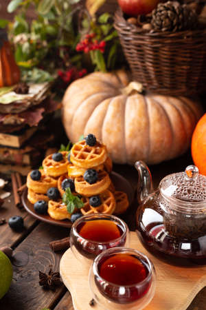 many waffles are stacked on a plate, decorated with mint leaves and blueberries. Tea in a glass teapot and two small bowls.の写真素材