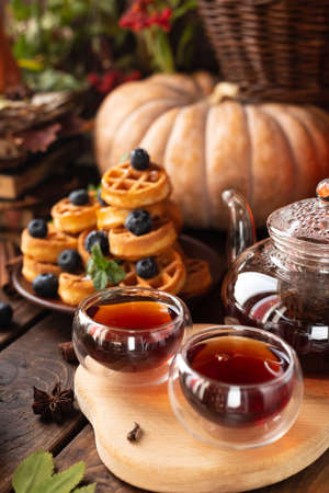 many waffles are stacked on a plate, decorated with mint leaves and blueberries. Tea in a glass teapot and two small bowls.の写真素材