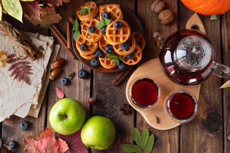 many waffles are stacked on a plate, decorated with mint leaves and blueberries. Tea in a glass teapot and two small bowls.の写真素材