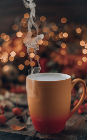 a red and yellow mug with a steaming drink. Fruits and spices are all around on a wooden table. lights of garlands are burning behindの写真素材
