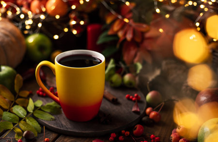 red and yellow mug with mulled wine. Fruits and spices are all around on a wooden table. lights of...