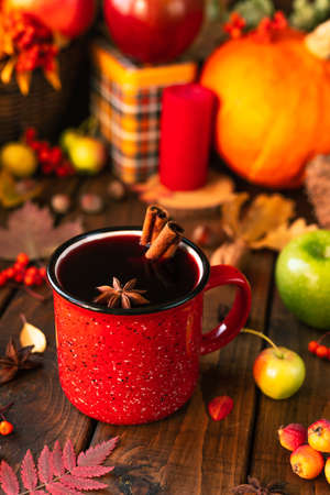 red mug with mulled wine. Cinnamon sticks stick out of the cup and a star of star anise floats. Fruits and spices are all around on a tableの写真素材