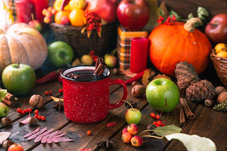 red mug with mulled wine. Cinnamon sticks stick out of the cup and a star of star anise floats. Fruits and spices are all around on a wooden tableの写真素材