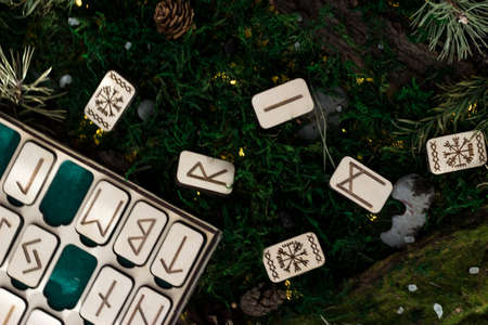 set of wooden runes in a box lie on the moss in the forest. rectangular wooden platforms on which Scandinavian runes are carved lie on green moss surrounded by salt, cones, fir needles and barkの写真素材