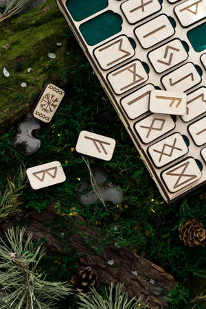 set of wooden runes in a box lie on the moss in the forest. rectangular wooden platforms on which Scandinavian runes are carved lie on green moss surrounded by salt, cones, fir needles and barkの写真素材