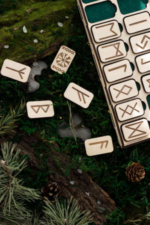 set of wooden runes in a box lie on the moss in the forest. rectangular wooden platforms on which Scandinavian runes are carved lie on green moss surrounded by salt, cones, fir needles and barkの写真素材