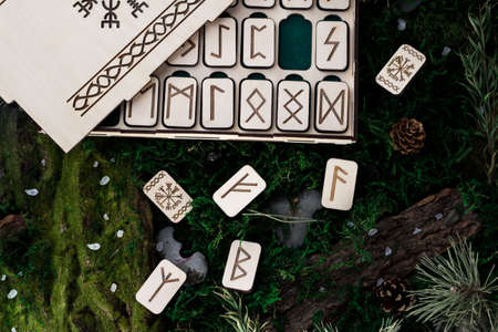 set of wooden runes in a box lie on the moss in the forest. rectangular wooden platforms on which Scandinavian runes are carved lie on green moss surrounded by salt, cones, fir needles and barkの写真素材