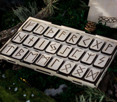 set of wooden runes in a box lie on the moss in the forest. rectangular wooden platforms on which Scandinavian runes are carved lie on green moss surrounded by salt, cones, fir needles and barkの写真素材