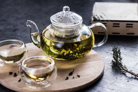 Yellow herbal tea in a transparent glass teapot and two bowls on a round wooden tray.の写真素材