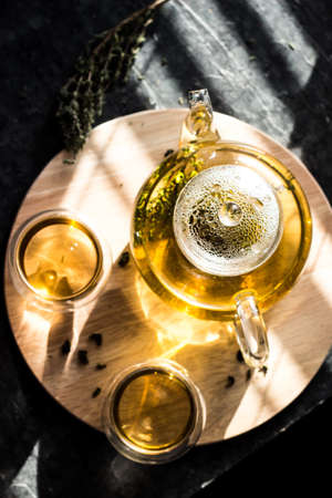 Yellow herbal tea in a transparent glass teapot and two bowls on a round wooden tray.の写真素材