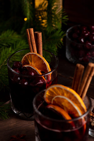 Two glasses on a wooden tray with mulled wine. Berries, orange slices and cinnamon sticks decorate...