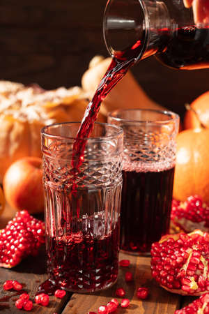 Two glasses are on the table among fruits and vegetables. A red liquid is poured into them from above.の写真素材