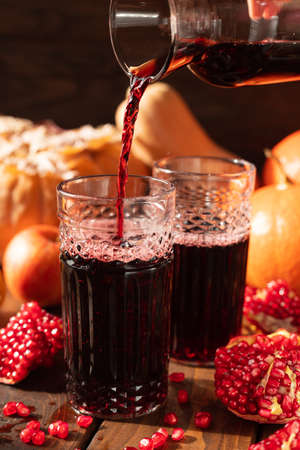 Two glasses are on the table among fruits and vegetables. A red liquid is poured into them from above.の写真素材