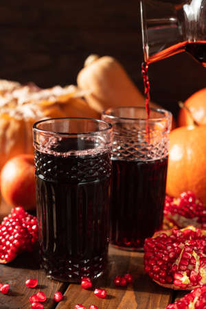 Two glasses are on the table among fruits and vegetables. A red liquid is poured into them from above.の写真素材