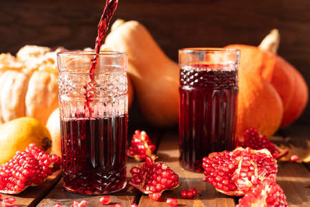 Two glasses are on the table among fruits and vegetables. A red liquid is poured into them from above.の写真素材