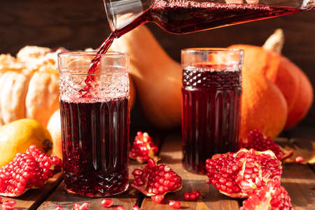 Two glasses are on the table among fruits and vegetables. A red liquid is poured into them from above.の写真素材