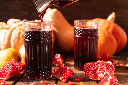 Two glasses are on the table among fruits and vegetables. A red liquid is poured into them from above.の写真素材