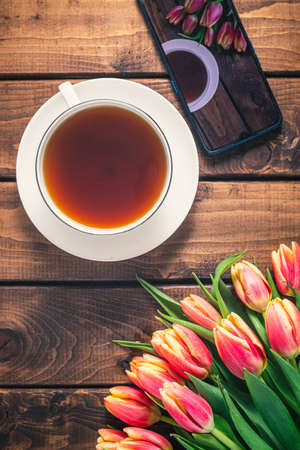 A bouquet of tulips lies on a wooden table next to a coffee mug.の写真素材
