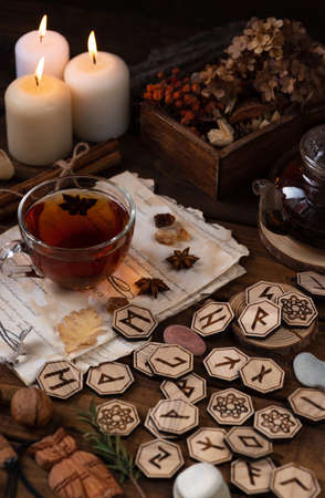 Wooden runes are lying on the table among the papers with notes. There is a mug of tea next to it. Astrology and esotericism.の写真素材