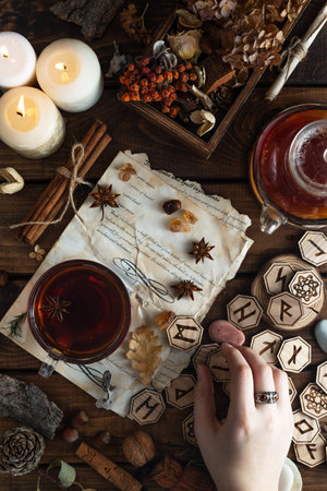 Wooden runes are lying on the table among the papers with notes. There is a mug of tea next to it....