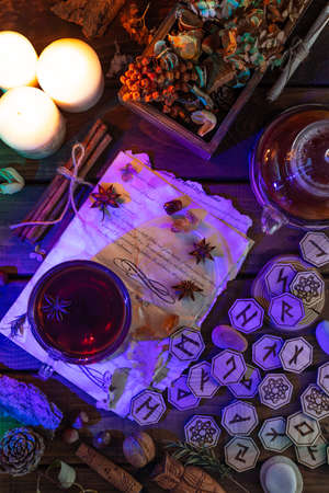 Wooden runes are lying on the table among the papers with notes. There is a mug of tea next to it. Astrology and esotericism.の写真素材