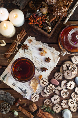Wooden runes are lying on the table among the papers with notes. There is a mug of tea next to it....