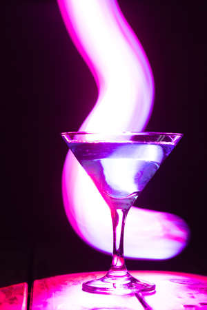 triangular glass with a blue cocktail on a dark background and neon lighting.の写真素材