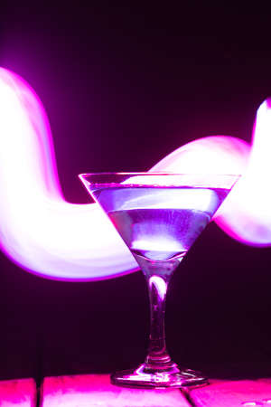 triangular glass with a blue cocktail on a dark background and neon lighting.の写真素材