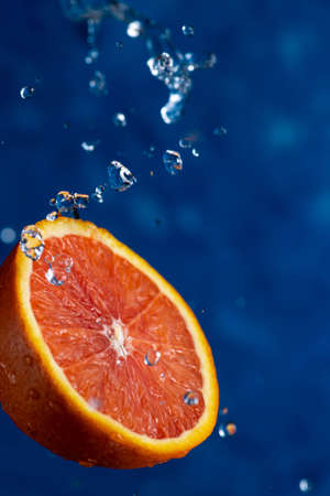 Half an orange falls on a blue background with drops of waterの写真素材
