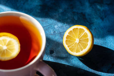 A mug with tea and lemon slices floating in it on a blue background.の写真素材