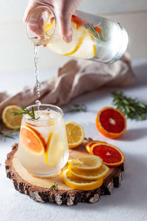 A glass and a decanter of lemonade. Lemon and grapefruit slices with rosemary leaves in a drinkの写真素材