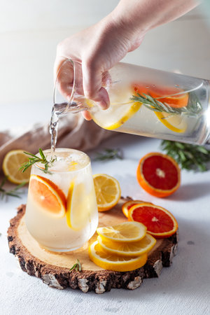 A glass and a decanter of lemonade. Lemon and grapefruit slices with rosemary leaves in a drinkの写真素材