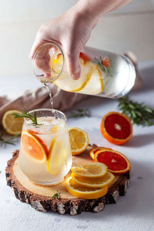 A glass and a decanter of lemonade. Lemon and grapefruit slices with rosemary leaves in a drinkの写真素材