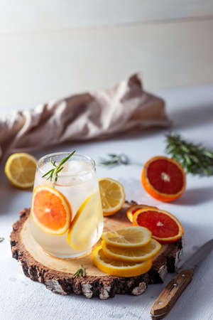 A glass and a decanter of lemonade. Lemon and grapefruit slices with rosemary leaves in a drinkの写真素材