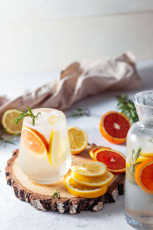 A glass and a decanter of lemonade. Lemon and grapefruit slices with rosemary leaves in a drinkの写真素材