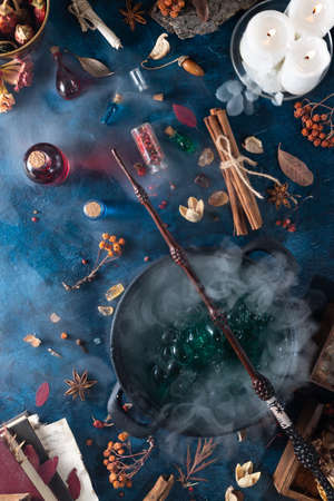 on the table is a cauldron with green a potion, a magic wand is on top. Ingredients are lying around and there are colorful bottlesの写真素材
