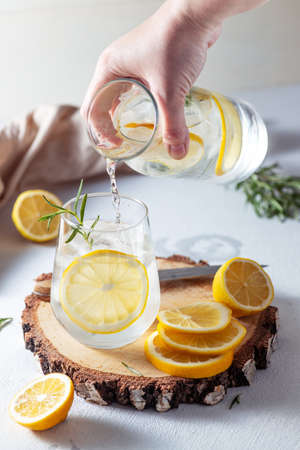 A glass and a decanter of lemonade. Lemon slices with rosemary leaves in a drinkの写真素材