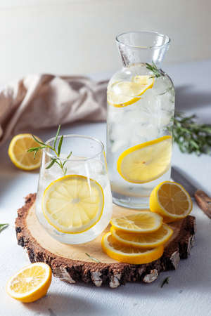 A glass and a decanter of lemonade. Lemon slices with rosemary leaves in a drinkの写真素材