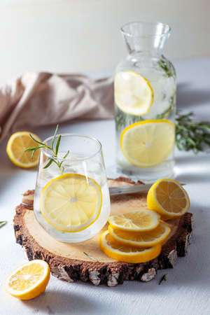 A glass and a decanter of lemonade. Lemon slices with rosemary leaves in a drinkの写真素材