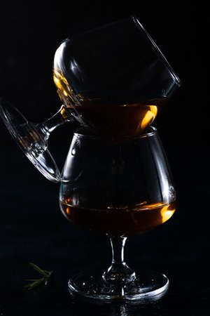 Two cognac glasses on a dark background. One is placed sideways on the otherの写真素材