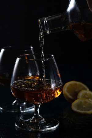 Two cognac glasses on a dark background. Cognac is poured into one glass from aboveの写真素材