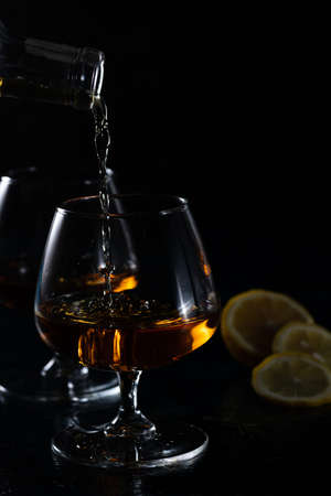 Two cognac glasses on a dark background. Cognac is poured into one glass from aboveの写真素材