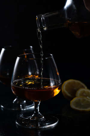 Two cognac glasses on a dark background. Cognac is poured into one glass from aboveの写真素材