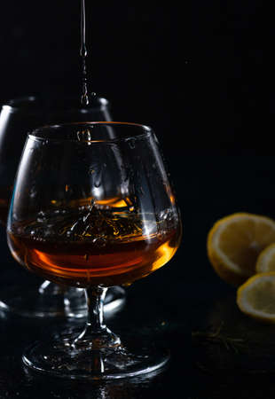 Two cognac glasses on a dark background. Cognac is poured into one glass from aboveの写真素材
