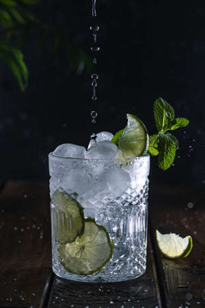 A clear carbonated drink in a glass glass with lime slices and fresh mint leaves.の写真素材