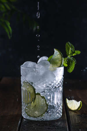 A clear carbonated drink in a glass glass with lime slices and fresh mint leaves.の写真素材