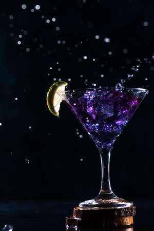 a cocktail glass with a drink inside stands on a stand with a slice of lime on the edge. neon trail behind the shot glassの写真素材