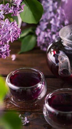Purple tea is poured from a glass teapot into cups. Lilac flowers are all aroundの写真素材